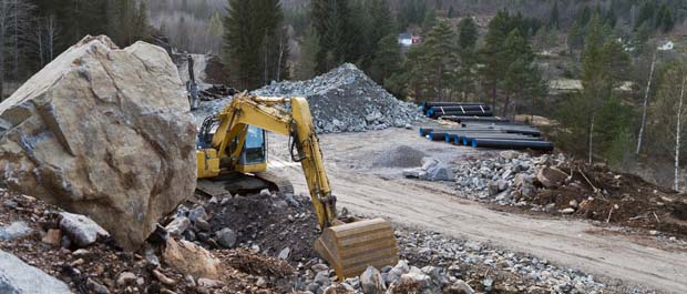 Bilde av en gul gravemaskin ved siden av en stor stein på et anleggsområde